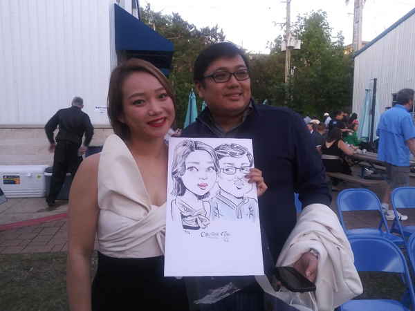Couple holding their handcrafted caricature to camera for picture created by our caricature artist Houston at outdoor event | Altus Entertainment